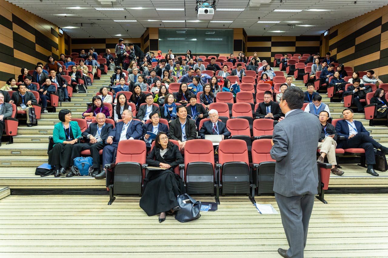 why-choose-us-02 Professional setting of a business conference with attendees and a presenter in an auditorium.